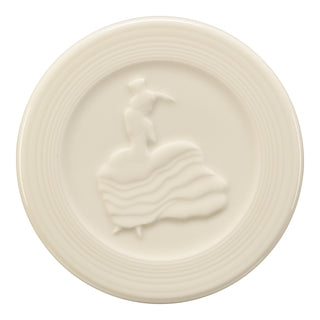 The Fiesta Linen Classic Rim 12-Piece Dinnerware Set W/Trivet features cream-colored plates with a classic rim, raised concentric ridges, and a central design of a woman in a flowing dress and hat.