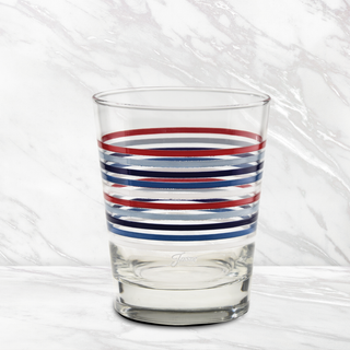 The Fiesta Americana Thin Stripe 15 oz. Tapered Double Old Fashion glasses by Moderne Glass feature alternating red and navy stripes and are made in the USA. The set of 4 is shown on a white marble surface with a matching marble background.