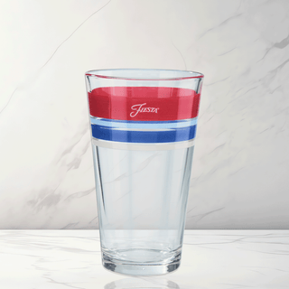 The Americana 16 oz. Edgeline Cooler Glass Set by Moderne Glass features red and blue stripes near the rim and "Fiesta" in white script, reflecting classic style. Set of 4. Made in the USA; shown on a white marble background.