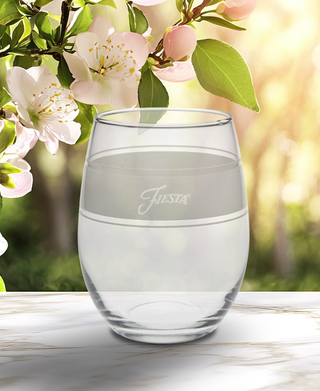 A set of four clear, 15 oz. Moderne Glass Linen Frame stemless glasses rests on marble, with white flowers and greenery behind. This elegant set is part of the iconic Fiesta Dinnerware collection and made in the USA.