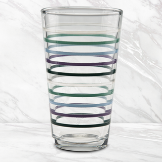The 16 oz. Fiesta Lavender Bloom Thin Stripe Cooler Glass by Moderne Glass features blue, green, and purple stripes on clear glass, shown on a white marble surface with a marble-patterned background. Set of 4. Made in USA.