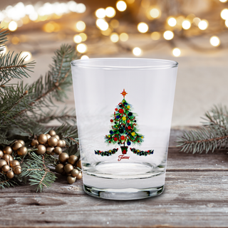 The 15 oz. Fiesta® Christmas Tree Tapered Double Old Fashion – Set of 4 by Moderne Glass features a festive tree design, displayed on rustic wood with pine branches, gold berries, and holiday lights softly glowing in the background.