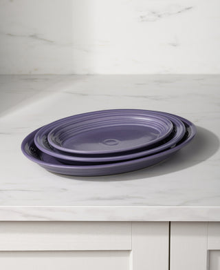The Fiesta Lavender 11 5/8 Inch Medium Oval Serving Platter rests on a white marble countertop with a white cabinet below, set against a light wall.