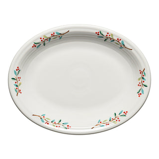 The Fiesta Retired Holly Berry Christmas 11 5/8 Inch Medium Oval Serving Platter features a white glossy ceramic finish with green leaves and red berries along the rim. This lead-safe china is perfect for festive holiday serving.