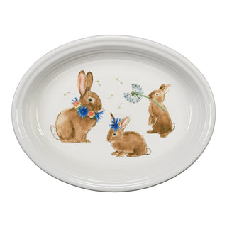 The Fiesta Retired Breezy Floral Easter 13 5/8" Oval Serving Platter features three brown bunnies with blue flowers and dandelions; one wears a flower crown, another a floral necklace, and one holds a dandelion. Made in the USA.