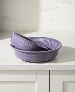 Two Fiesta Lavender Classic Rim 5 5/8 Inch Small Bowls (15 oz), made from lead-safe china and dishwasher safe, are stacked on a white marble countertop in a bright kitchen with white cabinets and a marble backsplash.