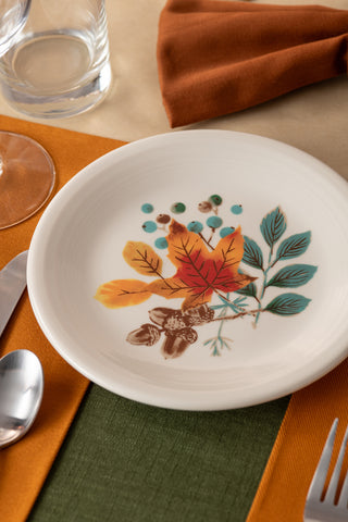 The Fiesta Autumn Fields Classic Rim 7 1/4 Inch Salad Plate, made in the USA and featuring a vibrant autumn leaf and berry design, is displayed on a table set with orange and green place mats, silverware, an orange napkin, and a glass.