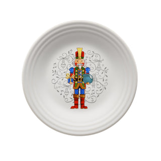 The Fiesta Nutcracker The Giver Classic Rim 9 Inch Luncheon Plate features a festive nutcracker design at the center, accented by gray musical notes, swirls, and Christmas ornaments.