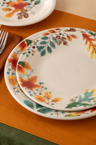 Three Fiesta Autumn Fields Classic Rim 10 1/2 Inch Dinner Plates, made in the USA from vitrified china and featuring colorful fall leaf designs, are stacked on an orange placemat with a brown napkin and fork nearby.