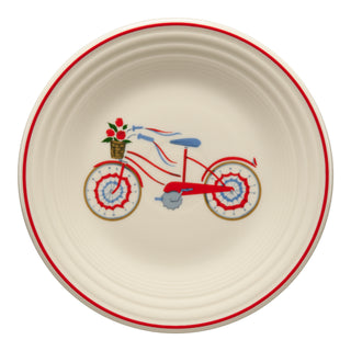 The Fiesta Americana Bicycle Classic Rim 9 Inch Luncheon Plate features a cream base, red rim, and a red bicycle with a basket of flowers and colorful wheel accents—perfect as patriotic dinnerware or an Americana plate.