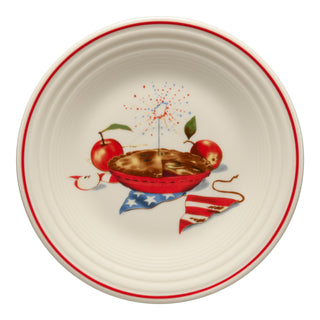 The Fiesta Americana Apple Pie Classic Rim 9 Inch Luncheon Plate features a red rim, an apple pie illustration, two apples, a flag napkin, and festive fireworks in the background.