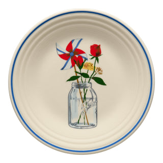 The Fiesta Americana Mason Jar Classic Rim 9 Inch Luncheon Plate features a cream design with a blue rim, showcasing a mason jar with a red rose, yellow flowers, and patriotic pinwheel—perfect for festive tables.