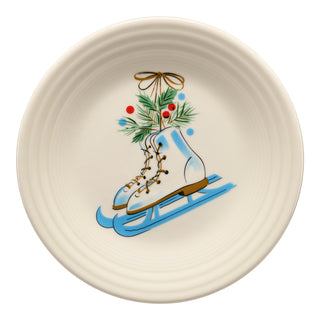 The Fiesta Jolly Christmas Skates Classic Rim 9 Inch Luncheon Plate features a festive design of white skates with gold laces on a blue sled, pine branches, red berries, and a gold ribbon from the Jolly Christmas Collection.