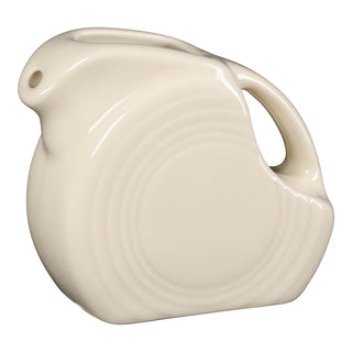 The Fiesta 5 OZ Mini Disk Pitcher by Fiesta features a linen-colored ceramic body, classic Art Deco design, curved handle, small spout opening, and signature concentric ring patterns.