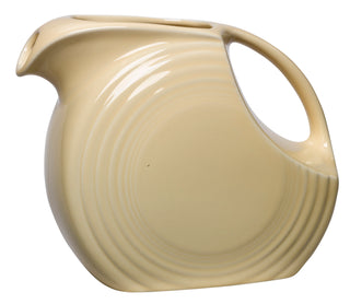 The Retired Fiesta 67 OZ Large Disk Pitcher by Fiesta features an art deco ivory ceramic design with horizontal ridges, a wide handle, and a color glaze. Proudly made in the USA with lead-safe china.