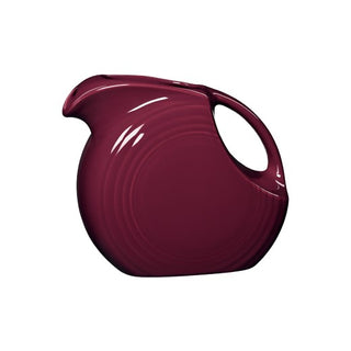 The Retired Fiesta 67 OZ Large Disk Pitcher by Fiesta features a glossy claret glaze, round body, wide base, open circular handle, curved spout, and subtle ridged detailing. Photo is on a plain white background.
