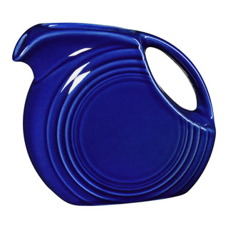 The Retired Fiesta 67 OZ Large Disk Pitcher by Fiesta, in twilight, features a round body, curved handle, small spout, and concentric circular ridges with a color glaze finish, displayed against a white background.