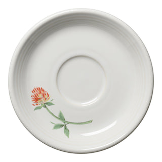 The Fiesta Retired Breezy Floral Classic Rim 5 7/8 Inch Saucer is made of durable vitrified china and features faintly ridged edges with a painted red and yellow clover flower and green leaves on one side.