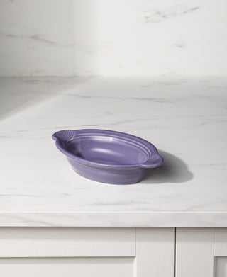 The Fiesta Lavender 9 1/8 Inch Oval Individual Casserole, 13 OZ, a purple ceramic dish perfect for oven-to-table use, rests on a white marble countertop with subtle gray veining and a white background.