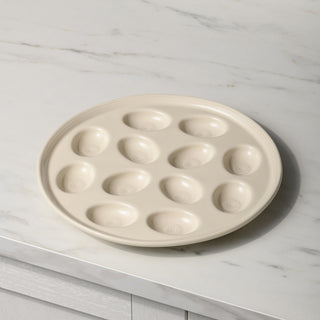 A beige Fiesta Round Egg Serving Platter, 11 1/4 inches across with twelve oval indentations for eggs, rests on a marble countertop.