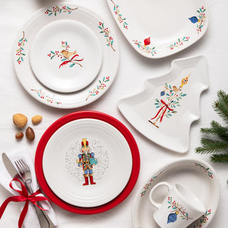 Fiesta Nutcracker The Giver Classic Rim 9 Inch Luncheon Plate displayed on a white cloth, with festive cutlery tied with red ribbon, a holiday-themed mug, tree-shaped platter, and pine accents for a cheerful Christmas table setting.