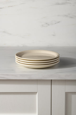 A Fiesta Linen Set of 4 Bistro Coupe 9 Inch Luncheon Plates is stacked on a white marble countertop with a white paneled cabinet below and a marble-patterned wall in the background.