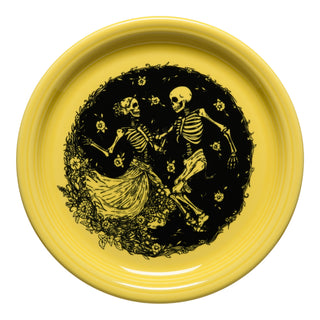 The Fiesta Retired Skeleton Duet Sunflower Bistro Coupe 9 Inch Luncheon Plate, made in USA, features a yellow base with a black illustration of two skeletons dancing amid flowers and leaves, evoking a festive Day of the Dead theme.