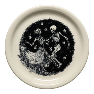 The Fiesta Skeleton Duet Linen Bistro Coupe 9 Inch Luncheon Plate features black art of two dancing skeletons—one in a long dress—amid floral motifs, all bordered by a circular floral design on cream vitrified china. Made in the USA.