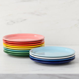 Two stacks of colorful plates sit on a white marble surface; the right stack features 9-inch Bistro Coupe Luncheon Plates by Fiesta in blue and white, all made in the USA.