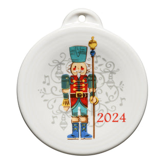 The Fiesta Retired Nutcracker Guardian 2024 Ornament is a round white ornament with a colorful nutcracker, musical notes, and bells. "2024" appears in red. Made from lead-safe china, it’s a charming keepsake for your collection.