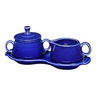 The Fiesta Retired 4-Piece Sugar Bowl and Creamer Set with Tray, in cobalt blue china with a glossy finish and decorative ridges, includes a lidded sugar bowl, creamer pitcher, and wavy-edged tray, all lead-safe.