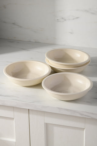 A set of four Fiesta Linen Classic Rim 8 3/8-inch, 34oz pasta bowls is arranged—two stacked, two side by side—on a white marble countertop with a light marble backsplash and white cabinetry in the background. Dishwasher safe ceramic.