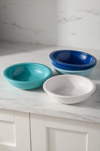 Three Mixed Coastal Blues Classic Rim 8 3/8-Inch 34oz Pasta Bowls from Fiesta, in teal, blue, and white, from a lead-free ceramic set of four, sit on a white marble countertop in a bright kitchen with white backsplash and cabinets.