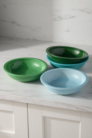 The Fiesta Mixed Aegean Classic Rim 8 3/8-Inch 34OZ Pasta Bowls, Set of 4, in green, dark green, teal, and light blue, are dishwasher safe and add vibrant charm to any kitchen. Perfect for displaying on a marble countertop.