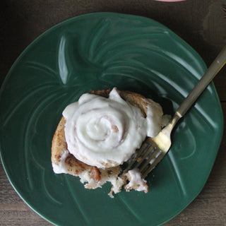 A cinnamon roll topped with white icing sits on a Fiesta Pumpkin Shaped Plate 8 1/2 Inch, with a fork beside it.
