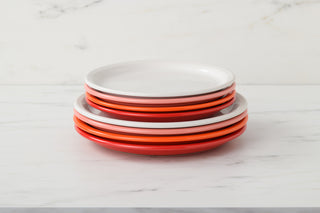 A stack of six Fiesta Bistro Coupe 9 Inch Luncheon Plates in red, orange, and white sits on a white marble surface. Each plate is beautifully crafted in the USA.