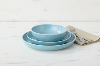 The Fiesta Coupe Bowl 3-Piece Place Setting, featuring light blue ceramic dishes—a coupe bowl, small plate, and large plate—rests on white marble. A beige napkin with a fork and knife sits beside this elegant arrangement.