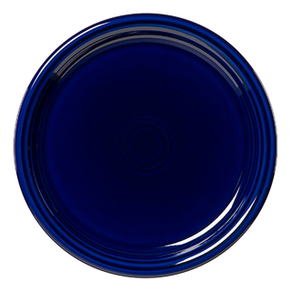 The Fiesta Retired Bistro Coupe 10 1/2 Inch Dinner Plate in cobalt blue features a round shape, glossy finish, and concentric ridges at the center. Crafted from lead-safe china, it’s shown from above on a white background.