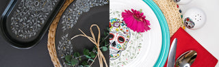 Two plates featuring colorful sugar skull designs, one dark and one white, are styled with utensils, a red napkin, flowers, and salt and pepper shakers, evoking a Day of the Dead theme.