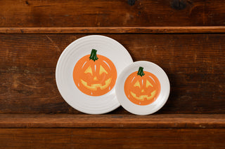 Two white plates with smiling jack-o’-lantern pumpkin faces are placed side by side on a wooden surface, with one plate larger than the other.
