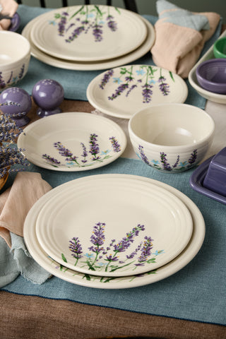 A table is set with the Fiesta Lavender Bloom Classic Bistro 3-Piece Dinnerware Set, Service for 1—each cream-colored plate and bowl adorned with delicate purple lavender motifs from the collection—surrounded by pastel napkins, purple salt and pepper shakers, and a blue placemat for a charming touch.