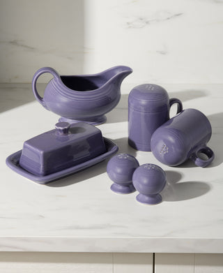 Set of purple ceramic kitchen items including a gravy boat, butter dish, and salt and pepper shakers on a white surface.