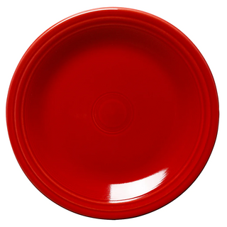 A round, bright red ceramic plate with a glossy finish and subtle concentric circle patterns near the rim, photographed on a white background.