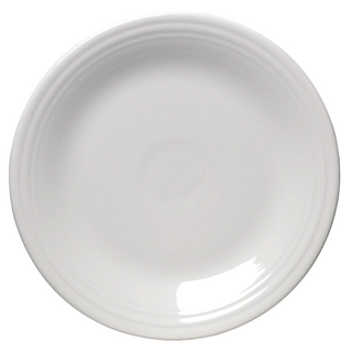 A plain, round, white ceramic plate photographed from above, showing a smooth, glossy surface with subtle concentric ridges near the rim.