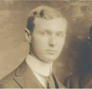 A sepia-toned vintage portrait of a young man with light hair, wearing a suit, high-collared shirt, and tie, posing against a plain, textured background.