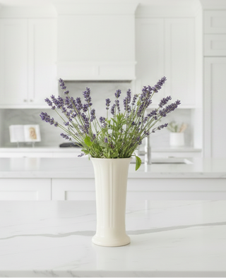 A bouquet of lavender flowers in the Fiesta Retired Linen Small Flower Vase (7.5" tall) sits on a marble countertop in a bright, white kitchen.