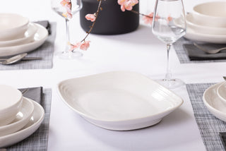 A close-up shows an elegant table setting with white ceramic dishes and bowls, the Fiesta 12 Inch Large Rectangular Platter by Fiesta, wine glasses on a white tablecloth, gray placemats, and pink cherry blossom branches.