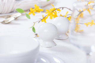 The Fiesta 2 5/8 Inch Salt and Pepper Shaker Set by Fiesta sits on a white tablecloth with yellow flowers and blurred tableware in the background, bringing classic Art Deco elegance to your tabletop.