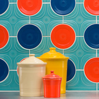 Three ceramic canisters—cream, yellow, and red—sit on a counter against a retro-style tiled wall with large red and blue circles and teal background patterns.