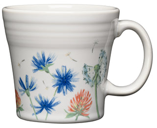 The Fiesta Retired Breezy Floral 15 OZ Tapered Mug is a white ceramic mug with a handle, featuring blue, red, and green wildflowers and dandelions; it’s dishwasher safe for easy cleaning.